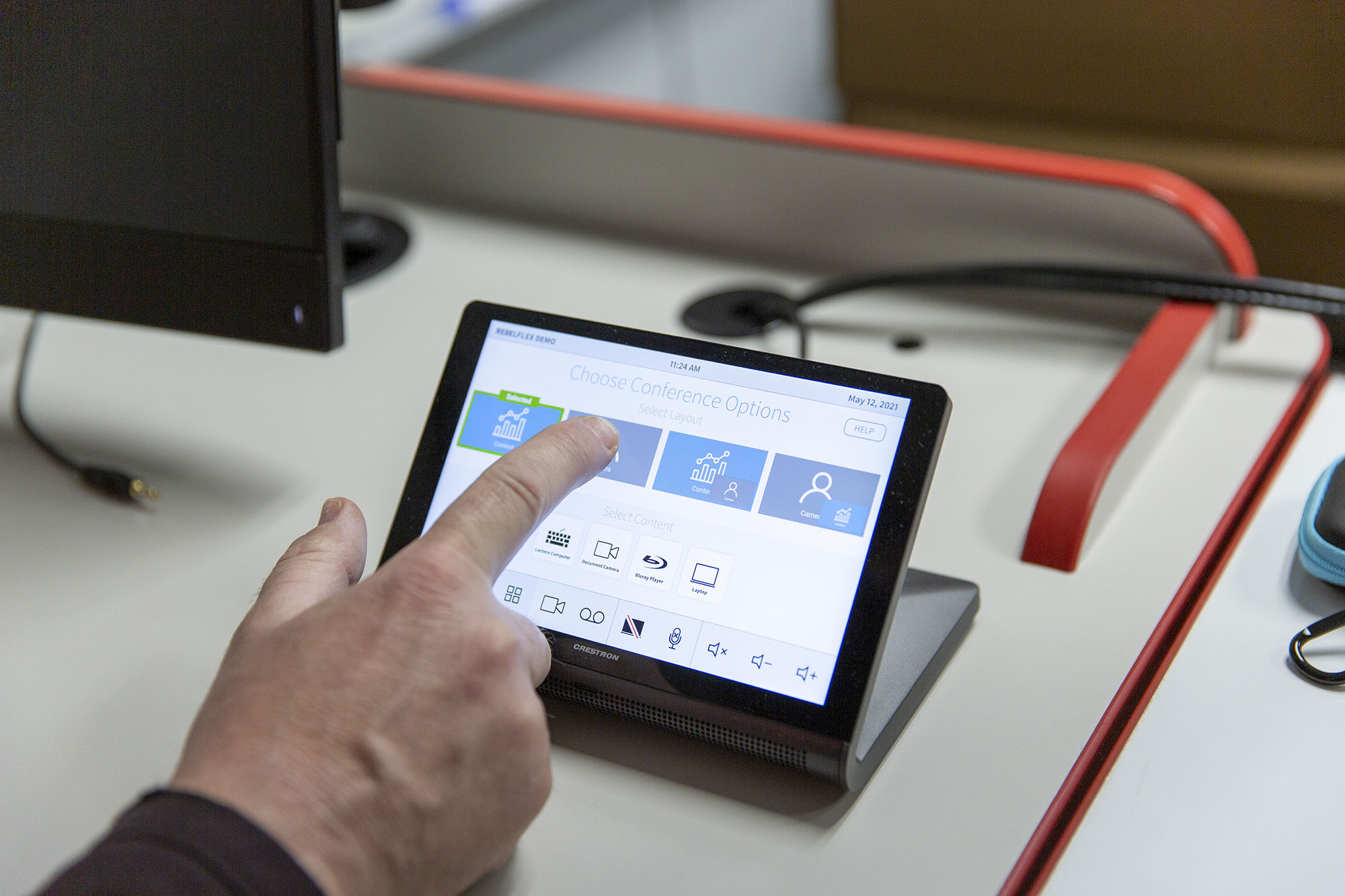 A finger reaches toward a UNLV classroom touch panel.