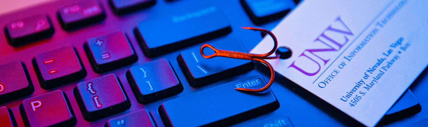 A U-N-L-V business card with a fish hook attached laying on top of a keyboard.