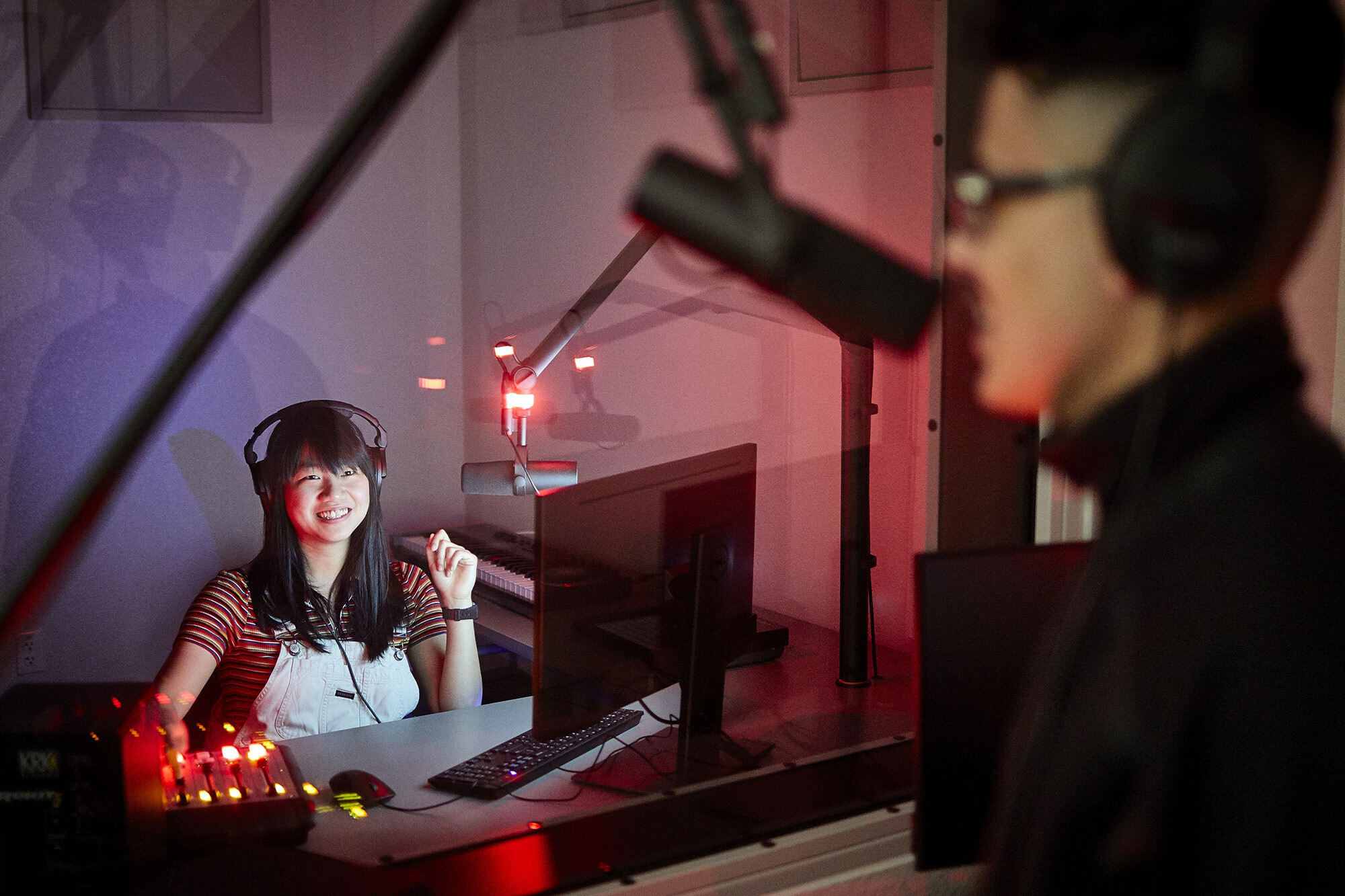 Person in a production booth speaking into a microphone.