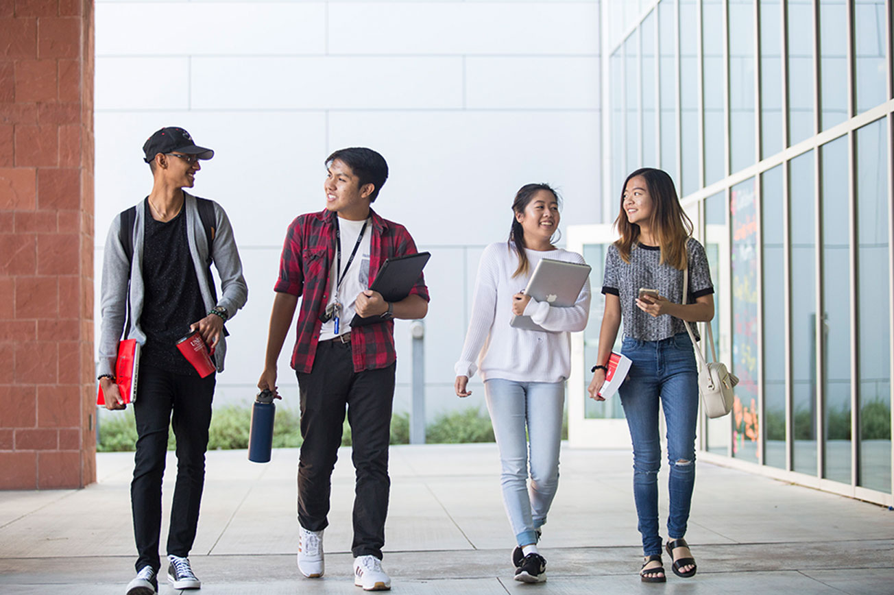 Four students side-by-side walking and smiling.