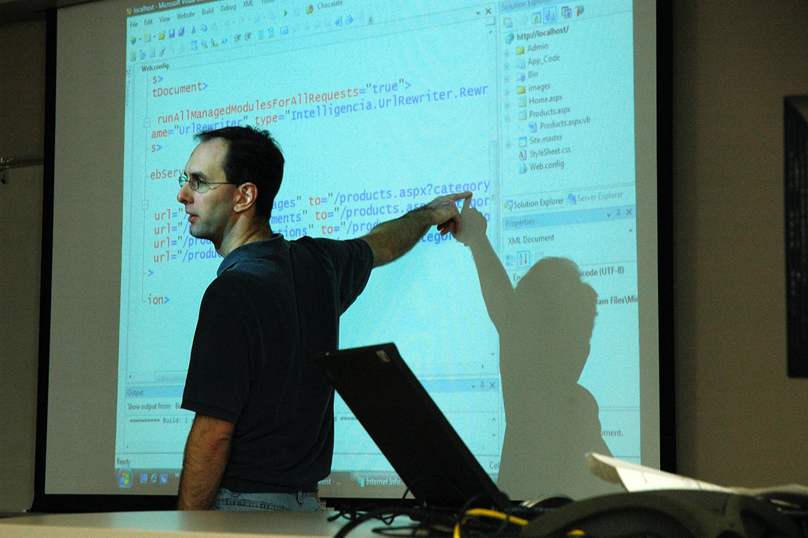 A male instructor points at a white board.