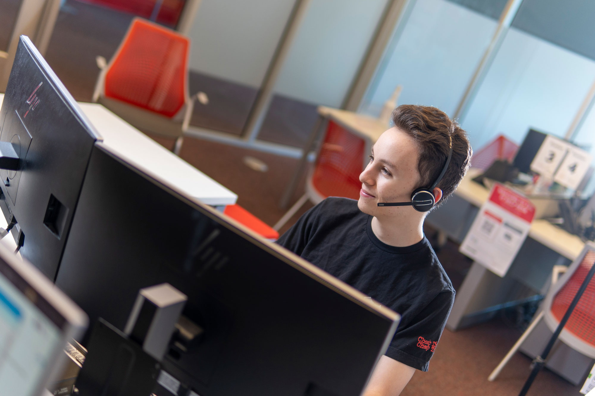 IT Help Desk student employee, wearing a headset behind a desktop computer.