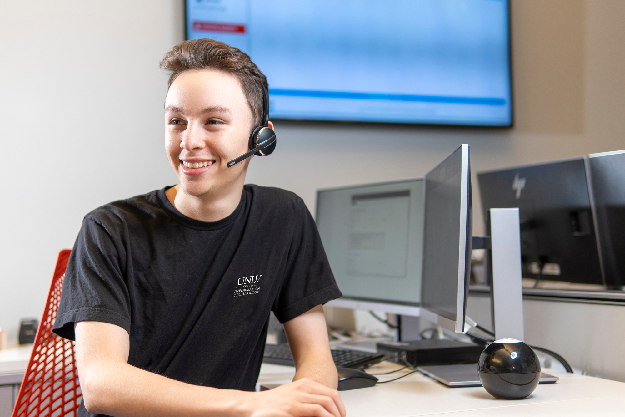 IT Help Desk student employee, wearing a headset behind a desktop computer.