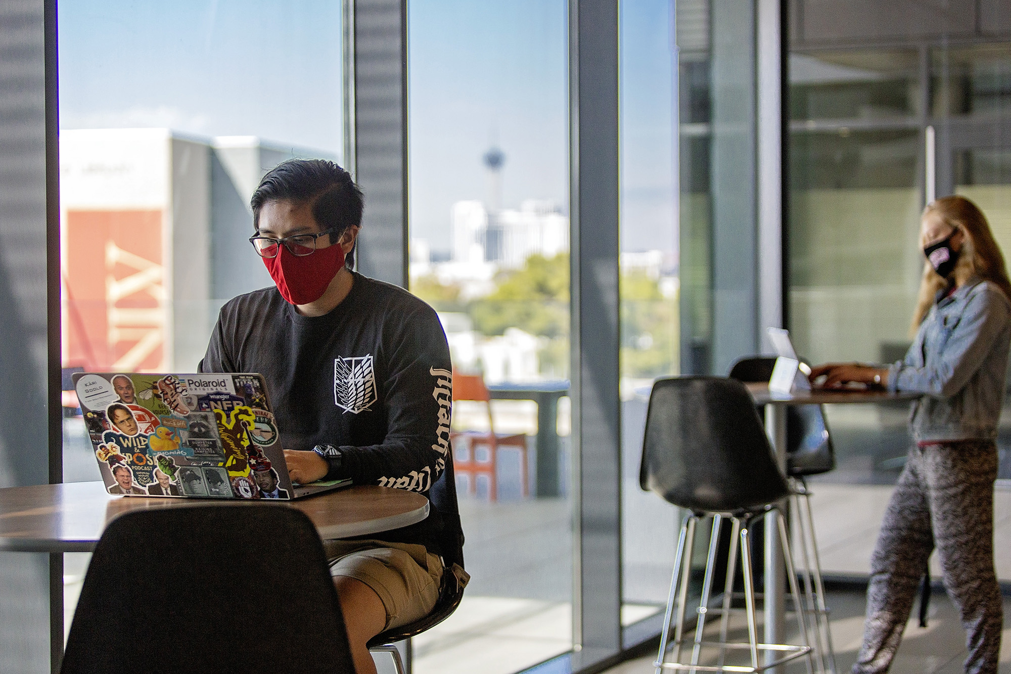 A student wearing a red face mask works on a laptop.