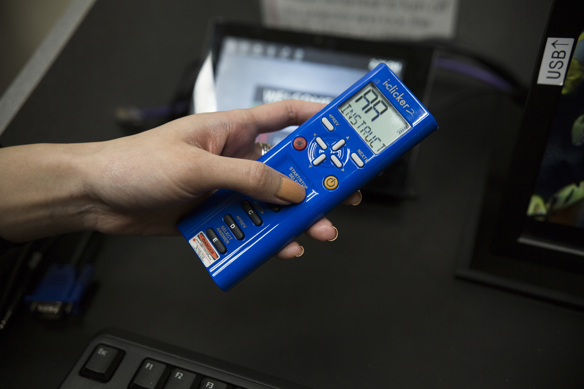 A hand holding a blue iClicker student remote.