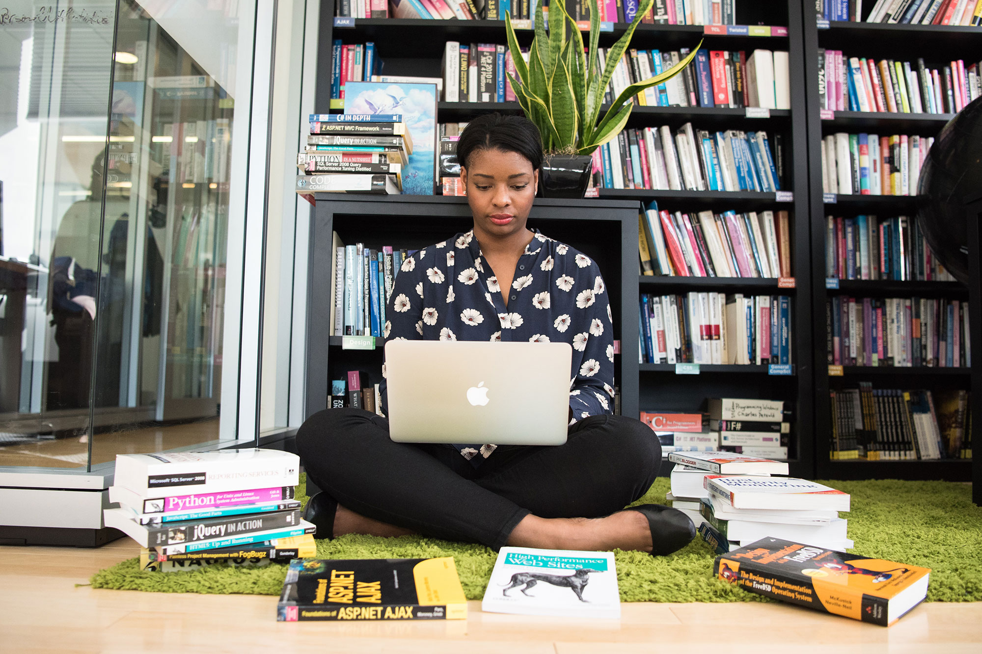 Student sitting on the ground using a laptop surrounded by books