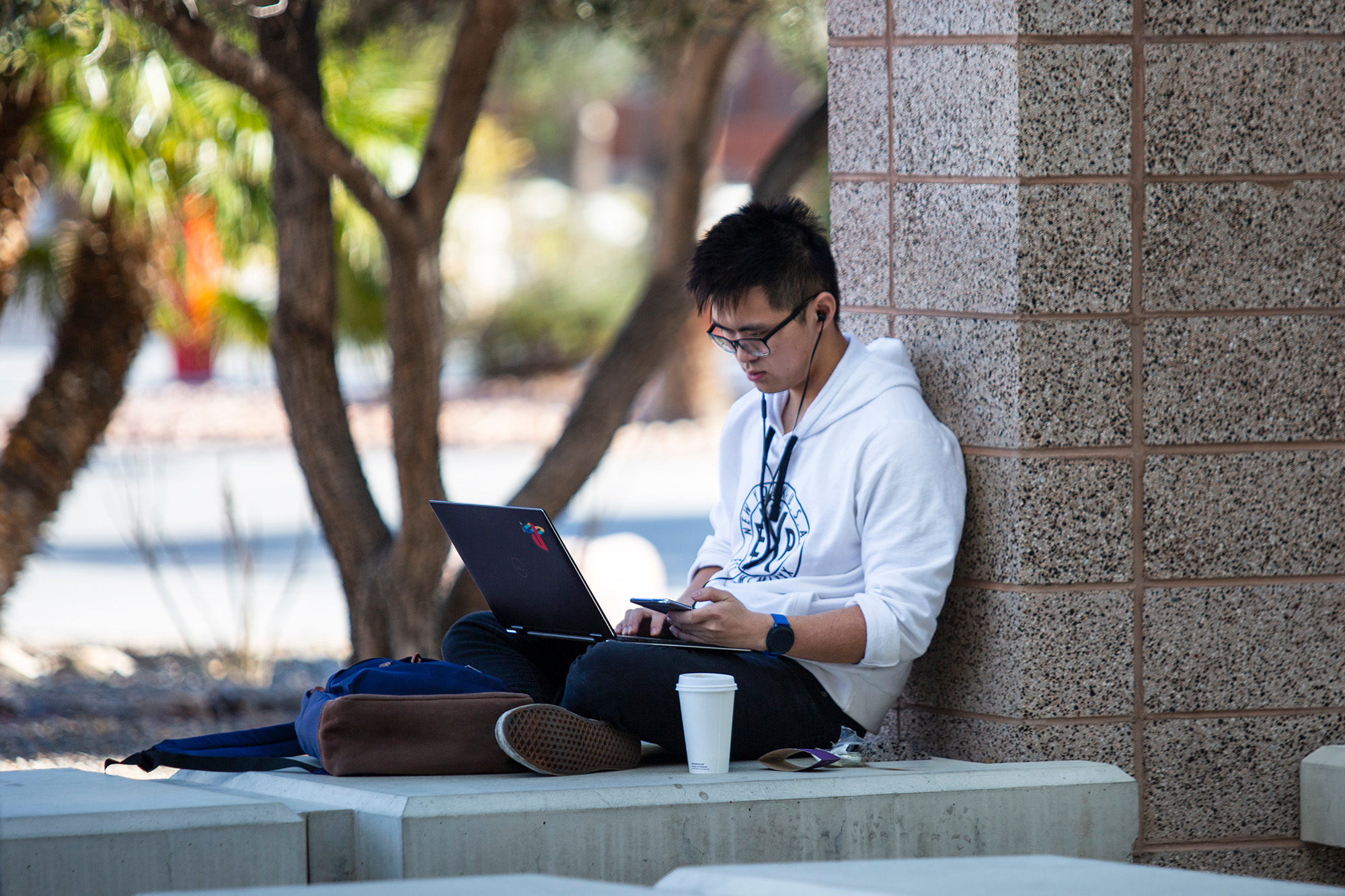 A student seated outside with his laptop and phone.