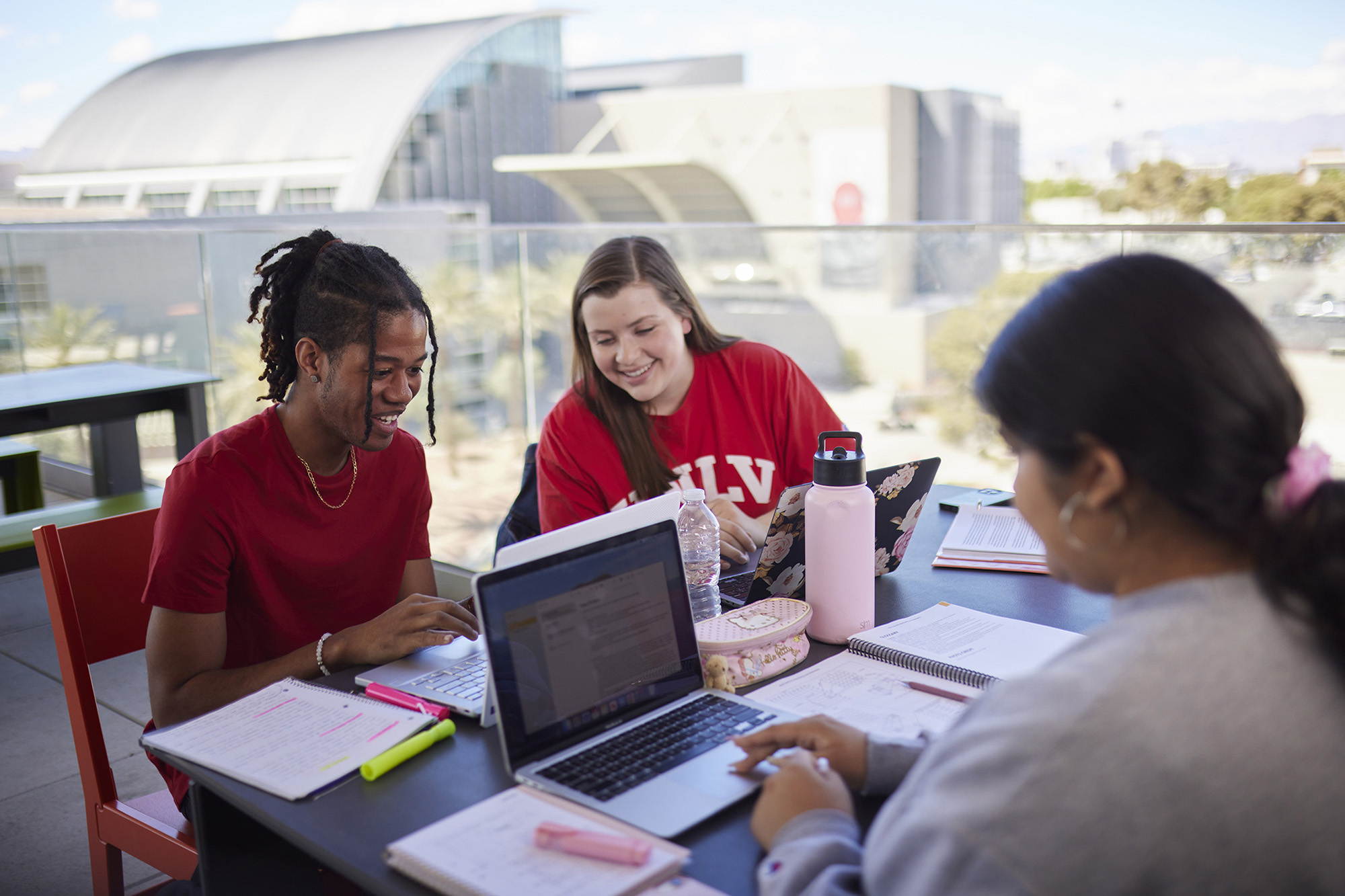 Students with laptops study outdoors with Lied Library in the background.