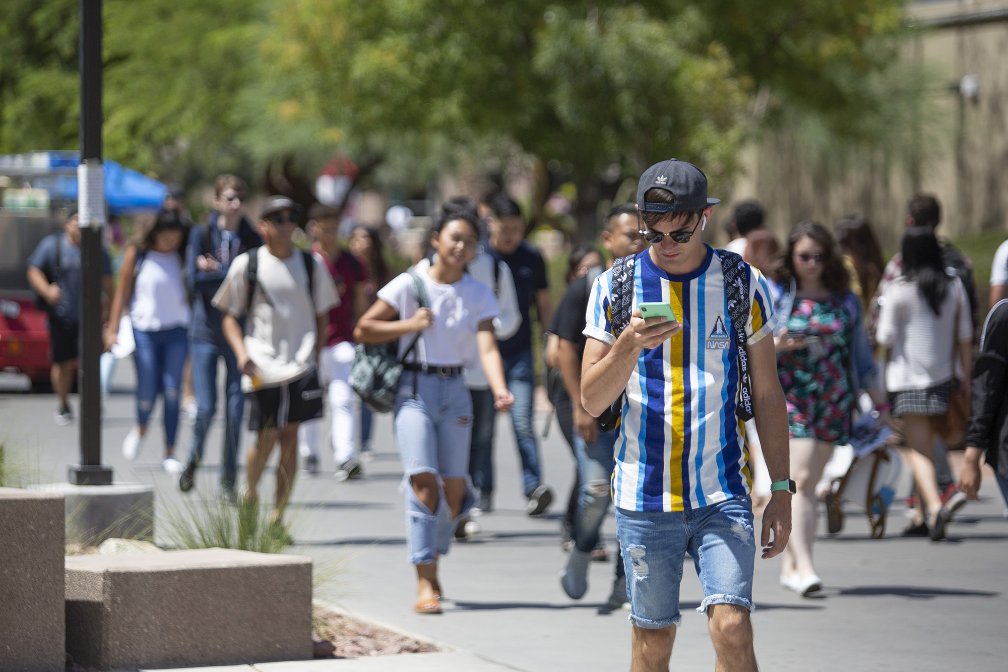 A male student looks down at his mobile device as he walks.