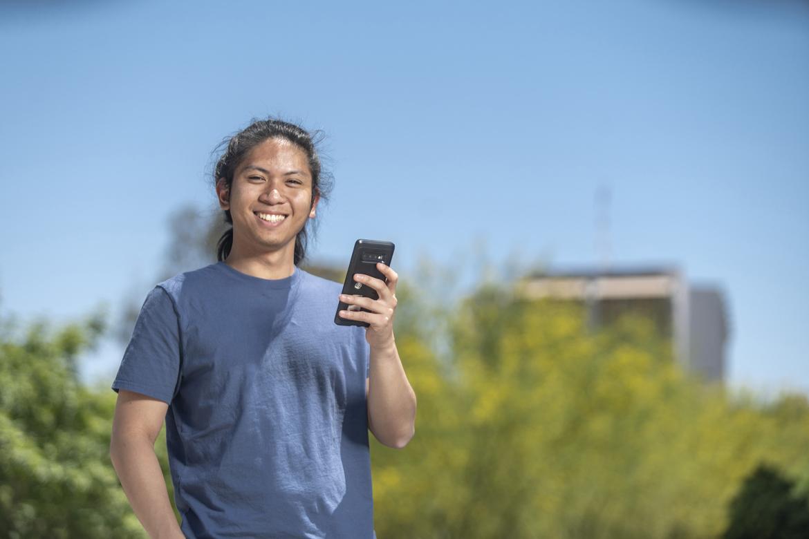 A smiling student poses holding a mobile device.