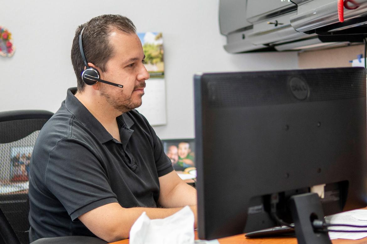 A UNLV employee wearing a headset at a computer desk.