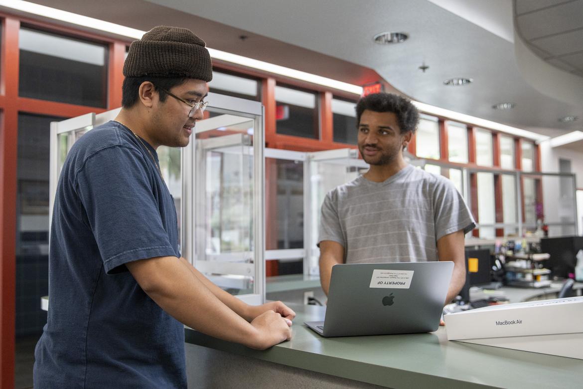 Two students look down at a laptop computer at the IT Help Desk.