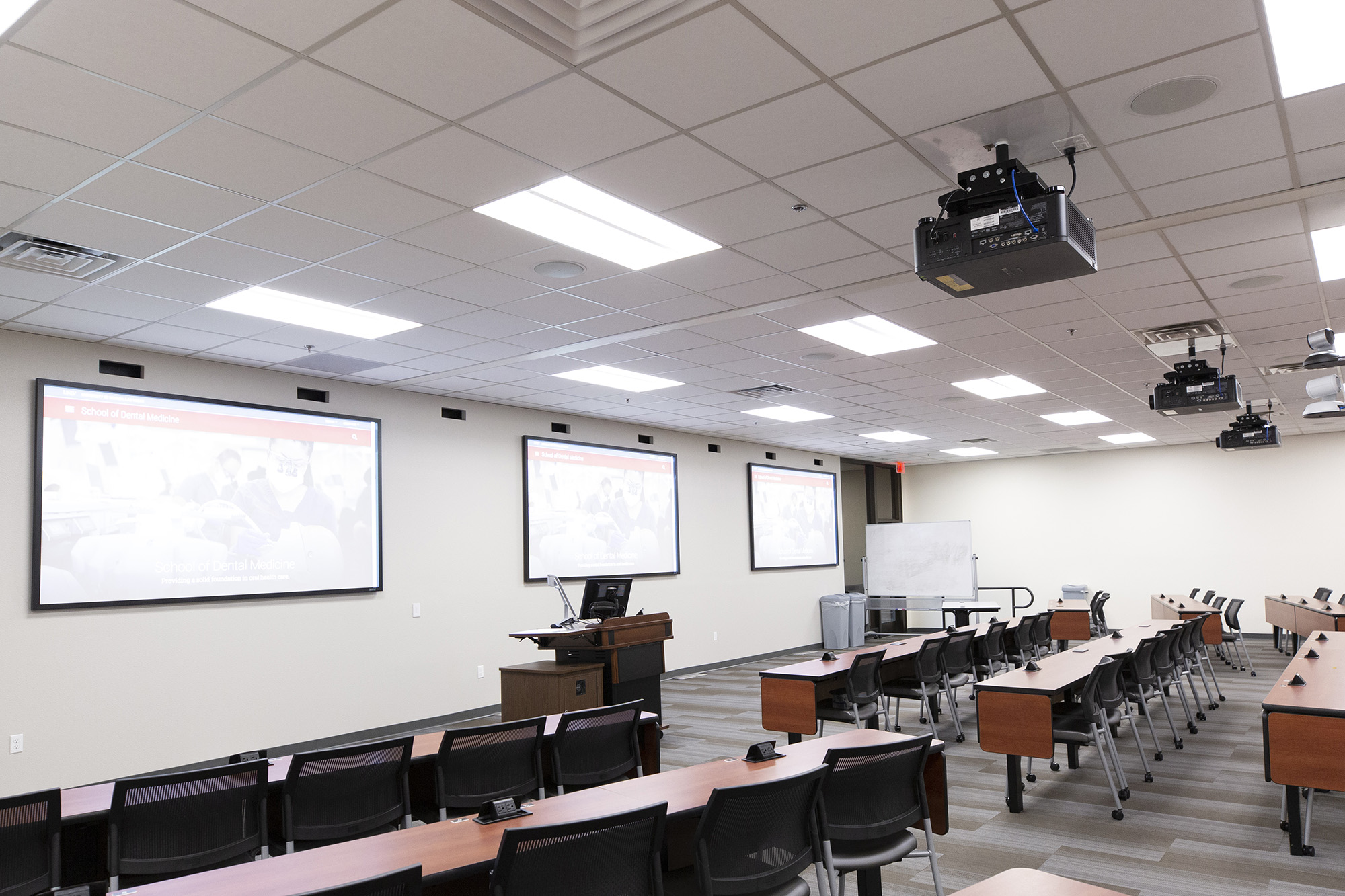 Rear diagonal view of three large projection screens in a U-N-L-V classroom.