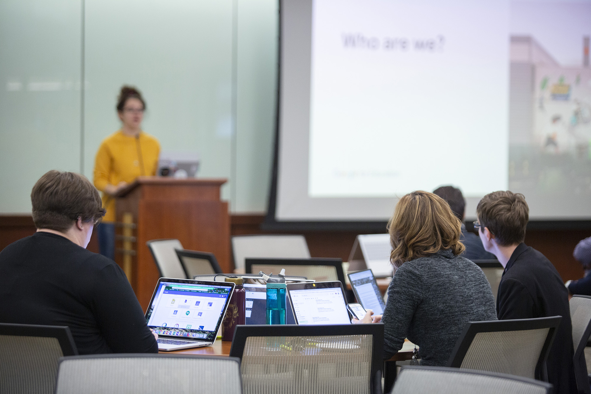 A group of people sitting at a table peer up at a speaker standing at a lectern.