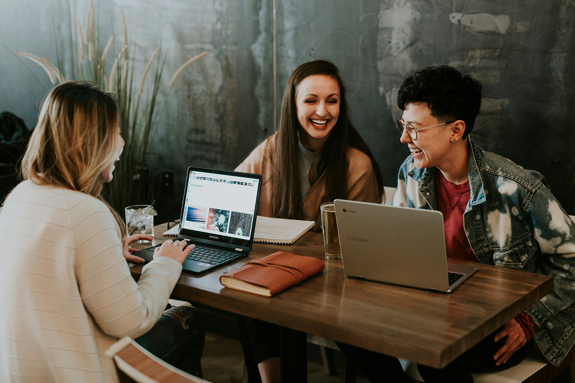 Three people studying at a wooden table enjoy a laugh together.