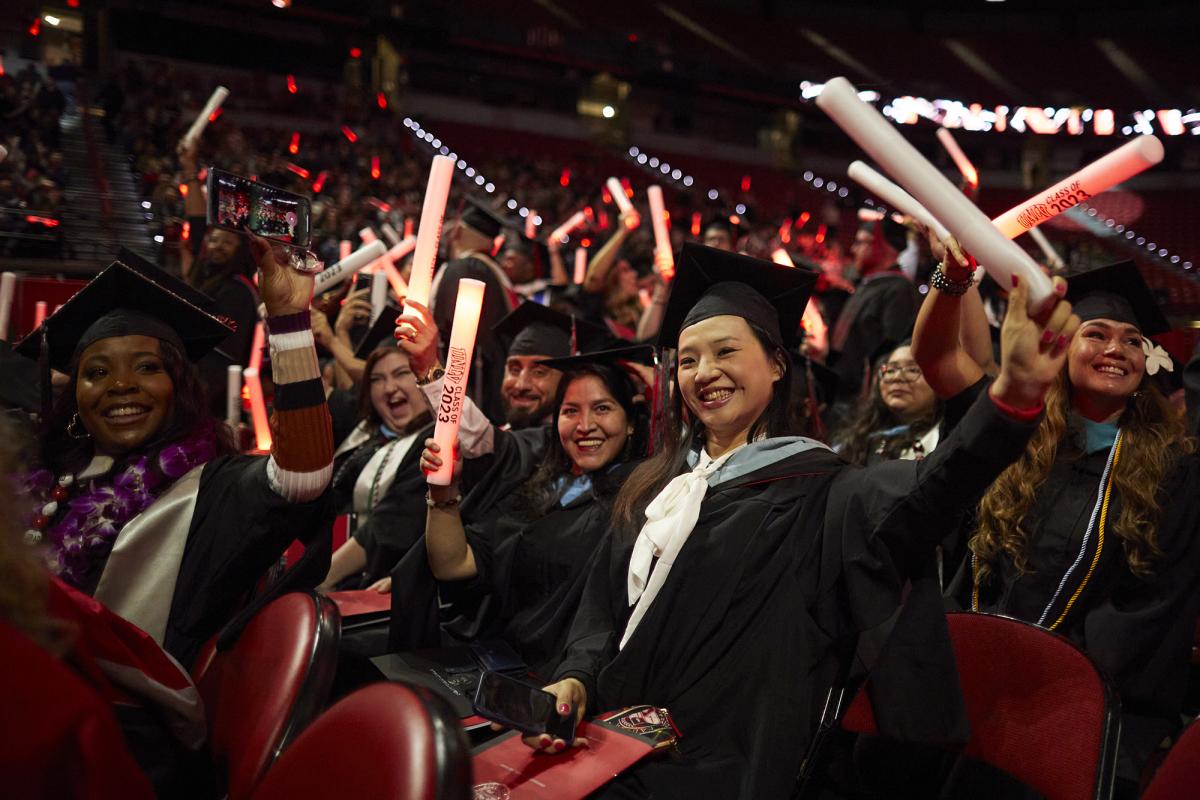 A group of smiling graduates hold up large, white glowing sticks.