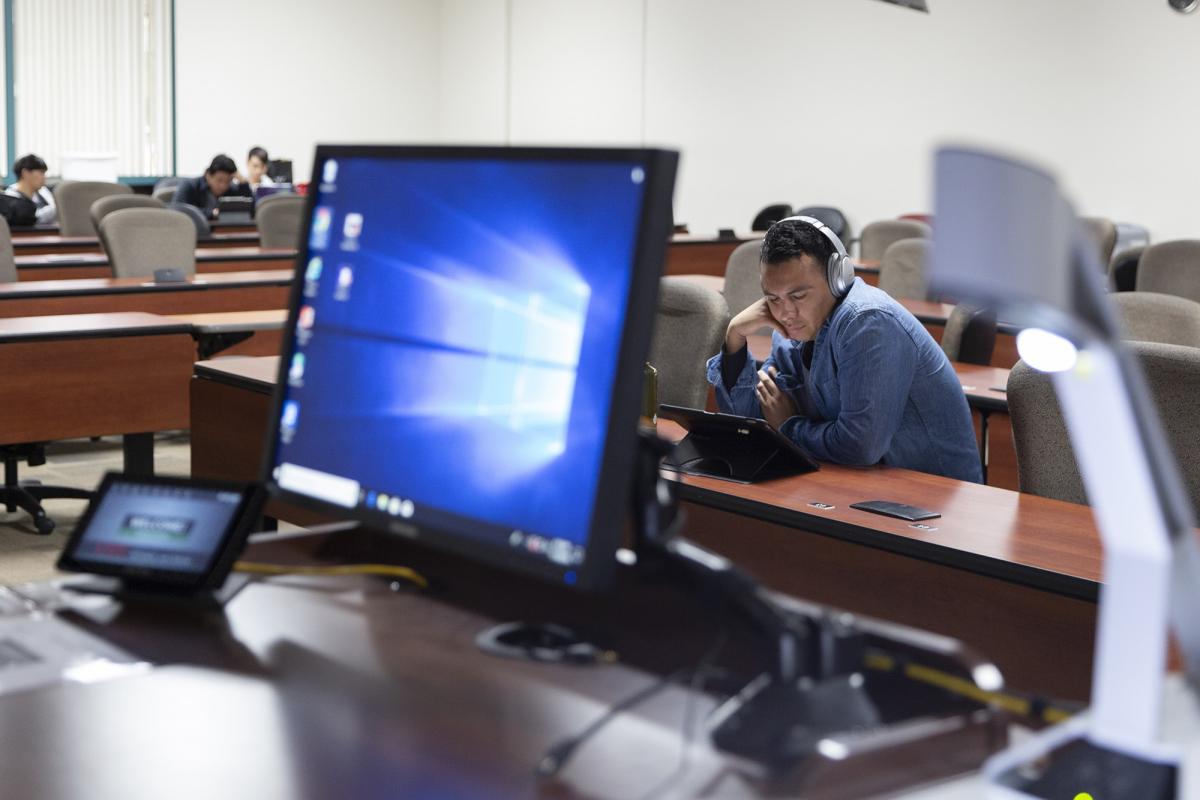 Lectern view of monitor display in classroom with student studying on tablet while wearing headphones.