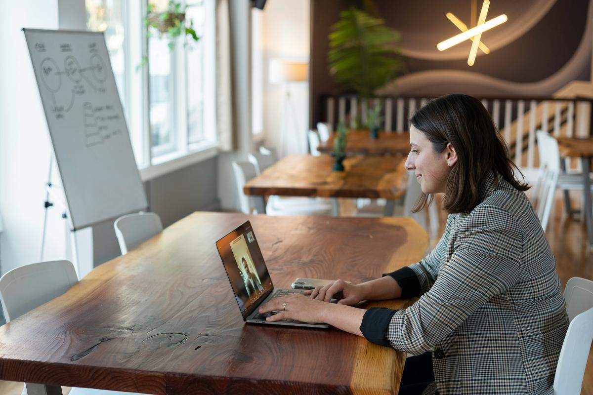 A person sitting at a wood table with an open laptop on a video call.
