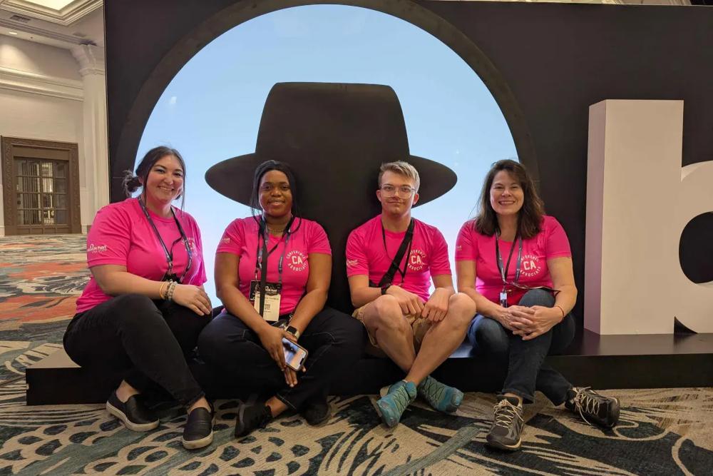Four people posing in front of Black Hat sign.
