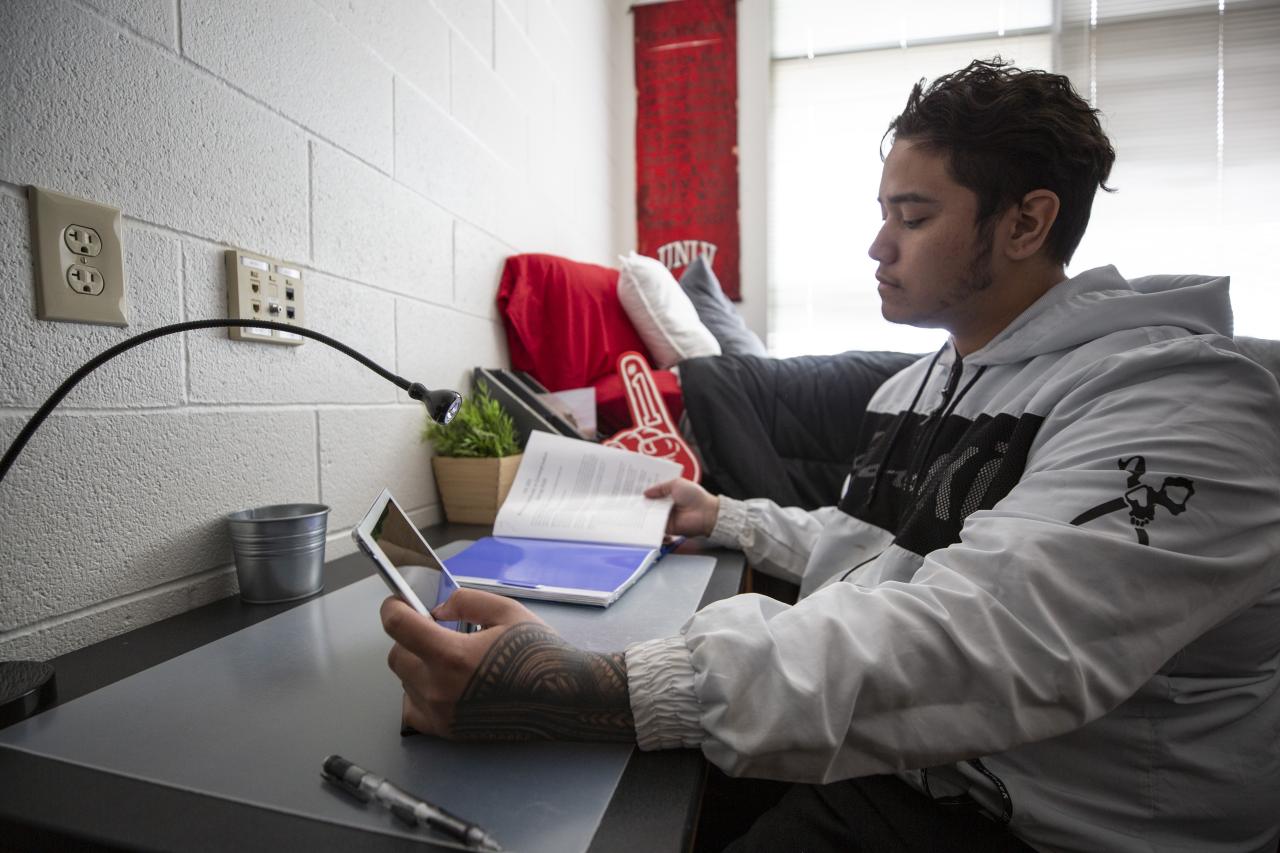A student using a tablet device in a campus dorm room.