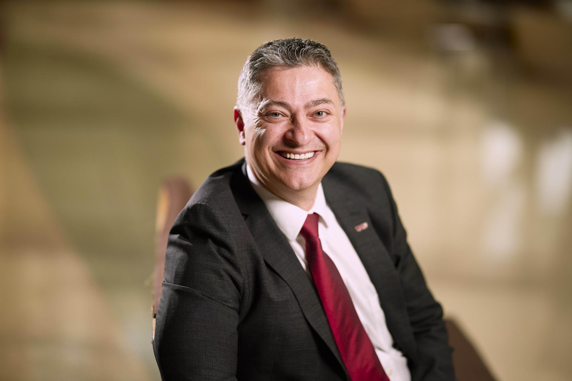 Person wearing a suit sitting down and smiling. 