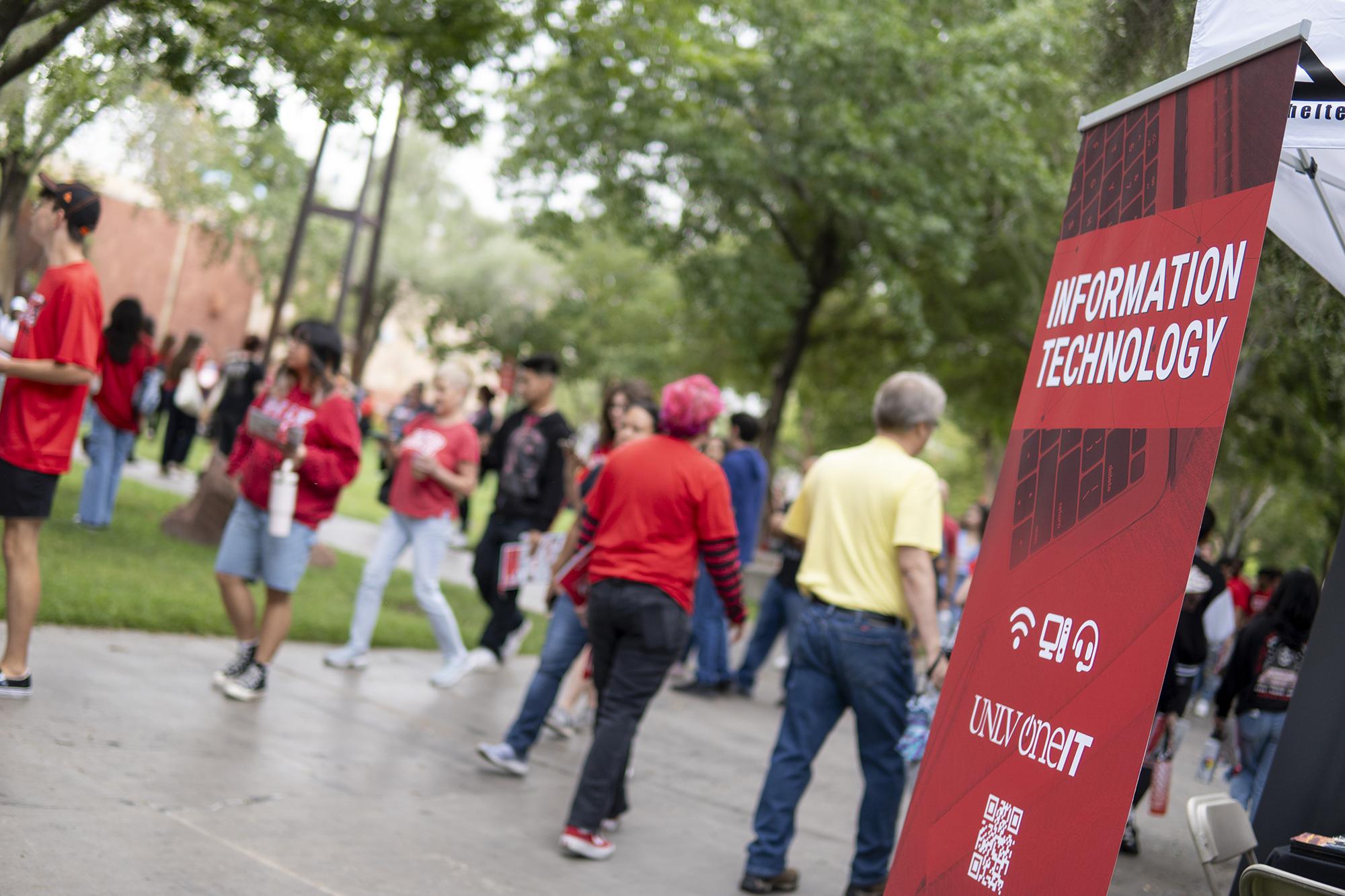 Groups of students walking past a red Information Technology banner. 