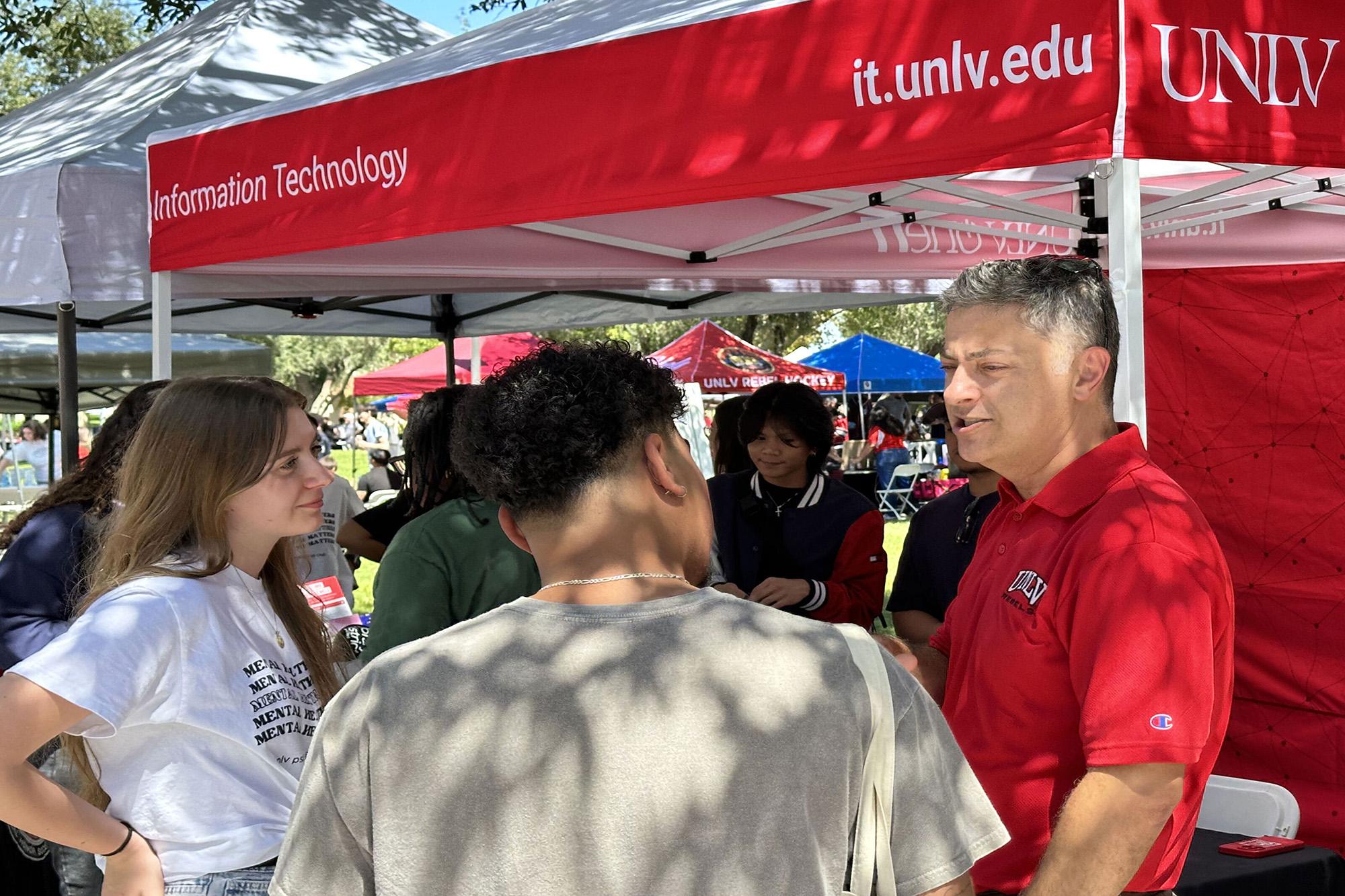 Person talking to two people near a tent that says information technology.