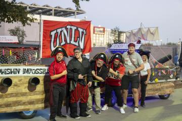 Group of people standing in front of two golf carts decorated as pirate ships with large flags.