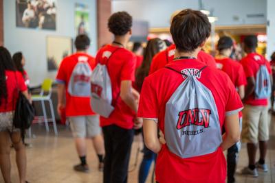 Student holding gray backpack with red UNLV letters.