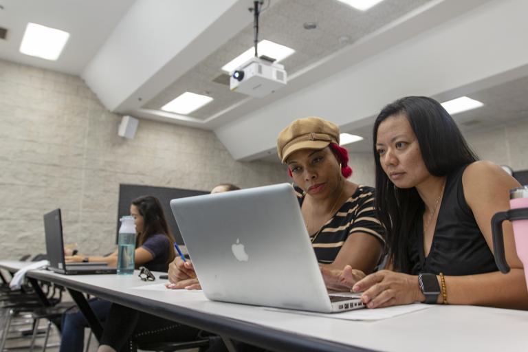 Two female staff members gaze at a laptop screen.