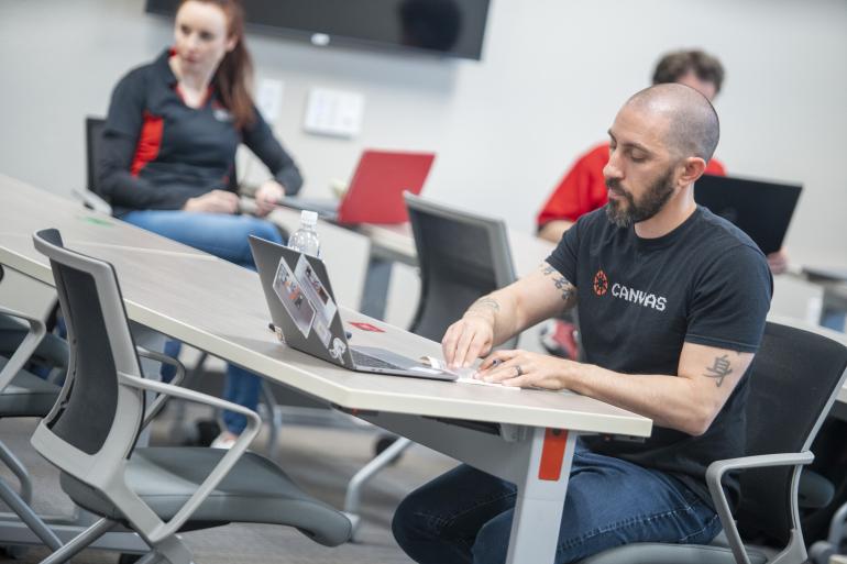 Person in black shirt sitting behind laptop at desk.