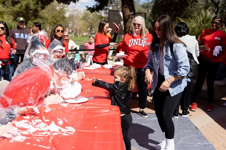 Child throws pie at person’s face as crowd watches on.