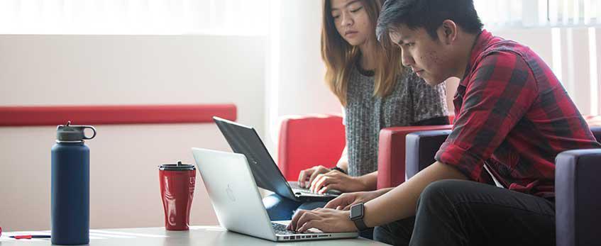 Two students study on their laptop computers.